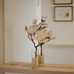 Zwei Vasen mit Magnolienblüten auf einer Ablagefläche vor einem Spiegel.