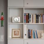 Bücherregal mit Uhr, Bilderrahmen und Dekoration. Wandhängendes Figurenobjekt neben Tür.