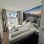 Schlafzimmer mit Doppelbett, Fenster und Wandbild. Holzboden und Nachttische.