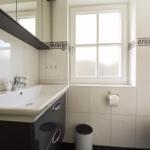 Badezimmer mit Waschbecken, Spiegel, Toilette und Fenster