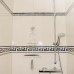 Dusche mit chromfarbenem Duschset und dekorativen Fliesenstreifen.