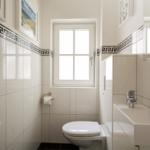 Badezimmer mit Toilette, Waschbecken und Fenster. Wandfliesen mit griechischem Muster.