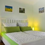Schlafzimmer mit weißem Bett, grünen Kissen und Wandbildern.