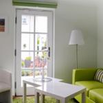 Ein Wohnzimmer mit grünem Sofa, weißer Couch und Fenster zur Außenterrasse.