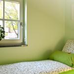 Ein Schlafzimmer mit grünen Wänden, einem Bett mit Kissen und einem Fenster mit Pflanze.