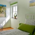 Schlafzimmer mit Bett, Fenster, Bildern und Kleiderständer.