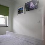 Ein Schlafzimmer mit weißem Bett, Wand-TV und Fenster mit grünem Rollladen.