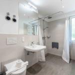 Badezimmer mit Dusche, Waschbecken und Toilette. Fenster und Heizung sind vorhanden.