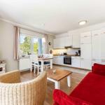 Wohnzimmer mit rotem Sofa, Esstisch und Küche im Hintergrund.
