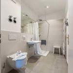 Badezimmer mit Dusche, Waschbecken und Toilette. Weiße Fliesen und modernes Design.
