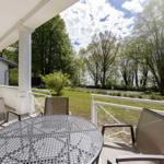 Terrasse mit Tisch und Stühlen, Blick auf Grünflächen und Bäume.