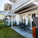 Terrasse mit Tisch, Stühlen und Liegestuhl neben Haus mit Balkon.
