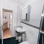 Badezimmer mit Dusche, Waschbecken und Heizkörper. Tür führt in Wohnbereich.