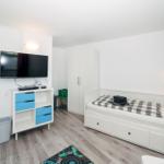 Ein Schlafzimmer mit Bett, Fernseher und Schrank. Holzboden und weiße Wände.