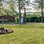 Grüner Garten mit Holzspielplatz, Rutsche und Schaukel. Im Hintergrund steht eine Holzhütte.