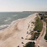 Strand mit Sand, Wellen und Strandkörben entlang einer Straße.