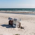 Strandkörbe mit Nummer 103 stehen auf dem Sand. Im Hintergrund das Meer.