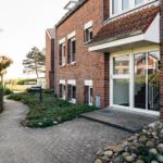Haus mit rotem Ziegelstein, Glasfront und gepflastertem Weg durch Grünanlagen.