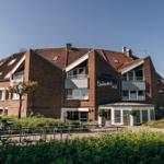 Ferienhaus Godewind mit rotem Ziegeldach und Balkonen. Grünanlage und Fahrräder vor dem Eingang.
