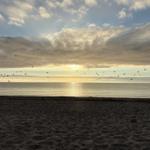 Strand bei Sonnenuntergang mit Vögeln im Himmel und ruhigem Meer.