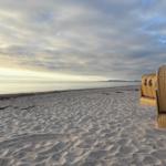 Strand mit Sandwellen und Strandkörben. Blick auf ruhiges Meer unter bewölktem Himmel.