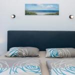 Doppelbett mit Kopfkissen und Bettwäsche mit Blumenmuster. Wandbild und zwei Nachttische mit Lampen.