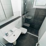 Badezimmer mit Dusche, Waschbecken und Toilette. Fliesen in Grau und Weiß.