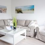 Wohnzimmer mit Sofa, Sessel und Tisch. Wandbilder zeigen Strand.