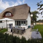 Haus mit Strohdach, Terrasse mit Tisch, Garten und Sonnenschirm.
