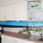 Küche mit weißen Schränken, Holz Arbeitsplatte und Küchenrückwand mit Strandmotiv.