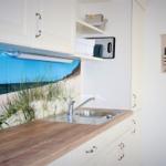 Küche mit Küchenzeile, Spüle und Küchenrückwand mit Strandmotiv.