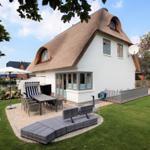 Wohnhaus mit Dach aus Stroh, Terrasse und Gartenbereich mit Sitzmöbeln.