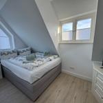 Schlafzimmer mit Dachschrägen, Bett, TV und Fenstern.