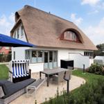 Haus mit strohgedecktem Dach und großem Gartenbereich mit Sitzmöbeln.