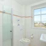 Badezimmer mit Dusche, Toilette und Waschbecken. Fenster mit Blick auf Außenbereich.