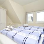 Zimmer mit Doppelbett, Kleiderschrank und Fenstern mit Blick auf Dächer.