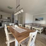 Essbereich mit Tisch und Stühlen, Küche und Wohnzimmer mit Sofa und Couchtisch.