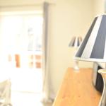 Tischlampe mit schwarz-weißem Schirm auf Holztisch. Im Hintergrund Tür und Stuhl.