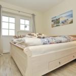 Schlafzimmer mit Bett, Nachttisch und Fenster. Wandbild zeigt Strand.