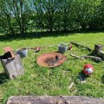 Grüner Garten mit Feuerstelle, Pflanzkübel und dekorativen Figuren.