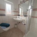 Badezimmer mit Dusche, Waschbecken und Toilette. Fenster mit Rollladen.