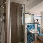 Badezimmer mit Dusche, Waschbecken und Toilette. Wandfliesen in Blau und Grau.