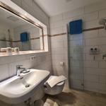 Badezimmer mit Dusche, Waschbecken und Toilette. Fliesenwand mit blauem Handtuch.