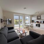 Wohnzimmer mit Sofa, Couchtisch und TV. Küche mit Esstisch und Fenster.