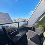 Terrace with two chairs and table, view of roofs and sky.