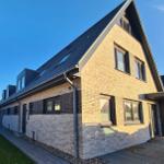 Modern villa with brick facade and dormers. Garden terrace and paved path.