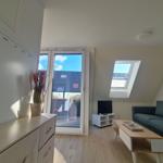 Wohnzimmer mit Sofa, TV und Balkonzugang. Holzboden und Dachfenster.
