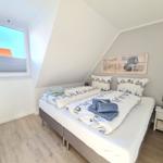 Schlafzimmer mit Doppelbett, Fenster und Nachttisch.