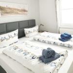 Schlafzimmer mit Doppelbett, Bettwäsche mit Strandmotiv und Fenster mit Vorhängen.