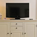 Flachbildfernseher auf einem weißen Schrank mit Schubladen und Türen.